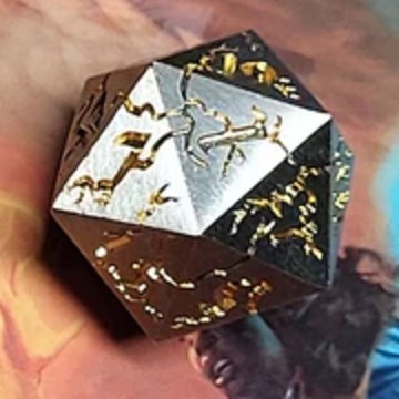 D20 — The Archer die, full scale: a brushed silver metal twenty-sided die with a gold archer constellation engraved across its triangular faces, cropped from the set photo